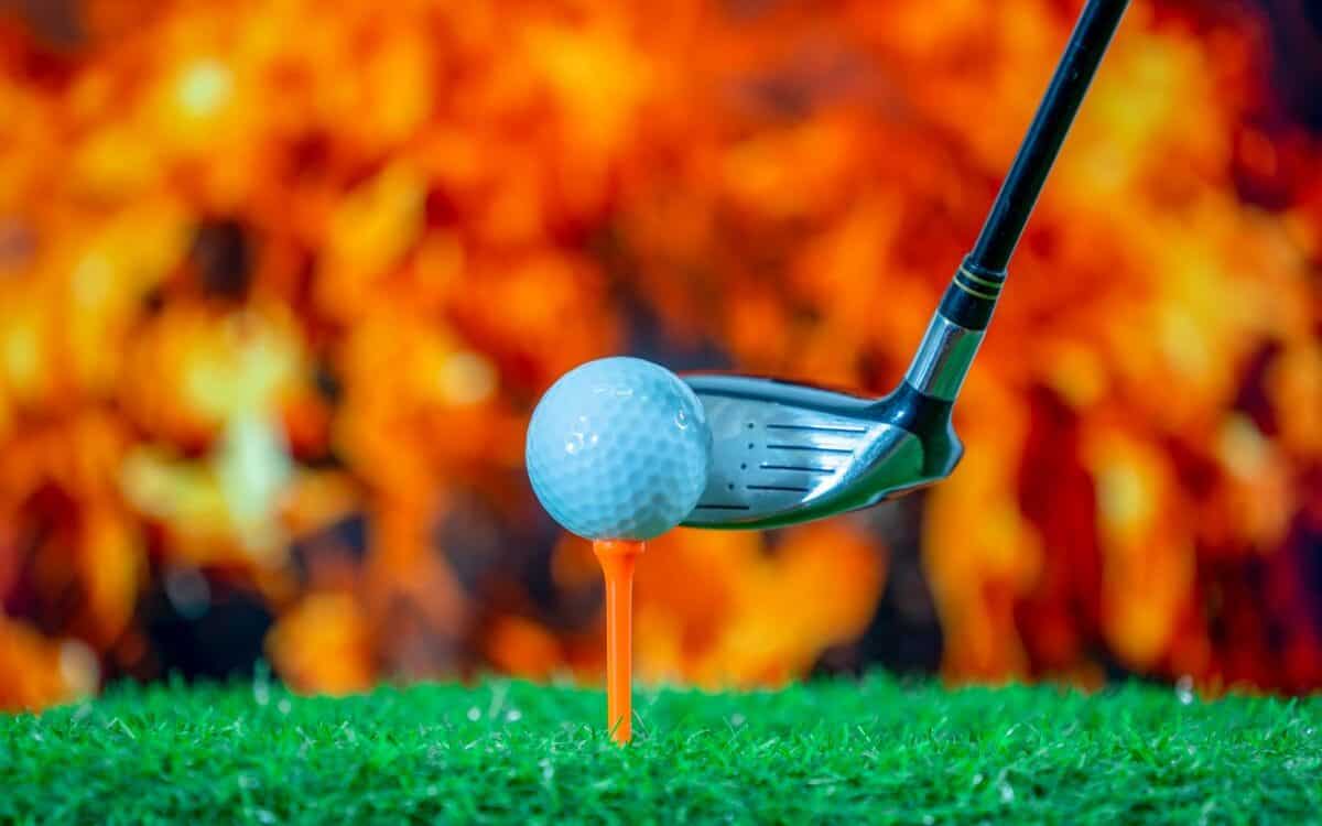 Golf ball on tee and golf club on blurred fire flame background