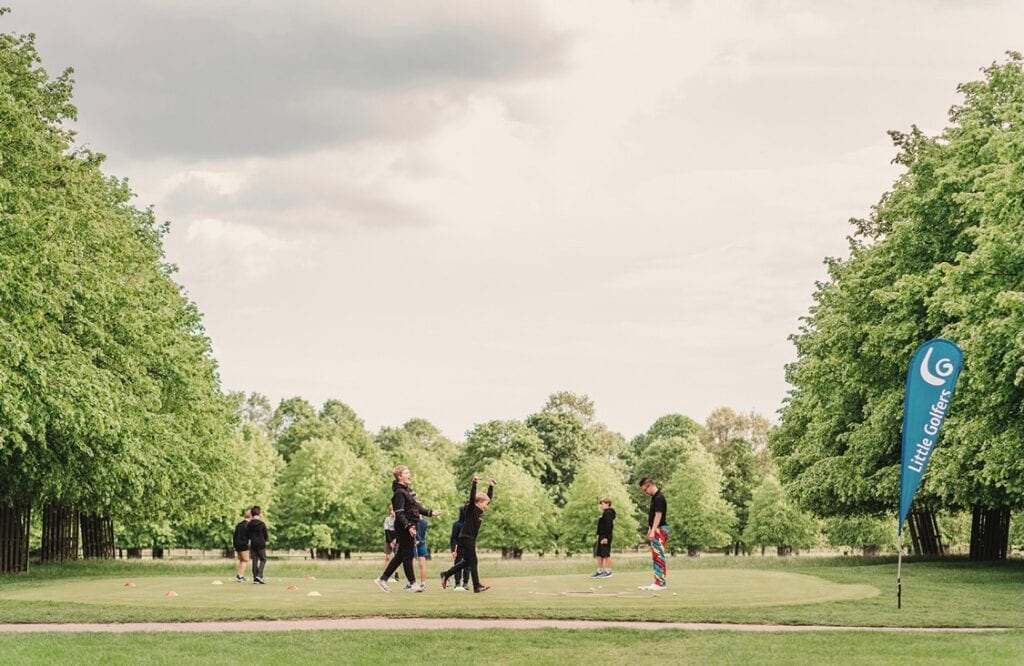 Andy Little, online golf coach, founder of Little Golfers and the first English PGA pro to earn U.S. Kids Golf Master Kids Coach status overseeing a junior golf class on a putting green